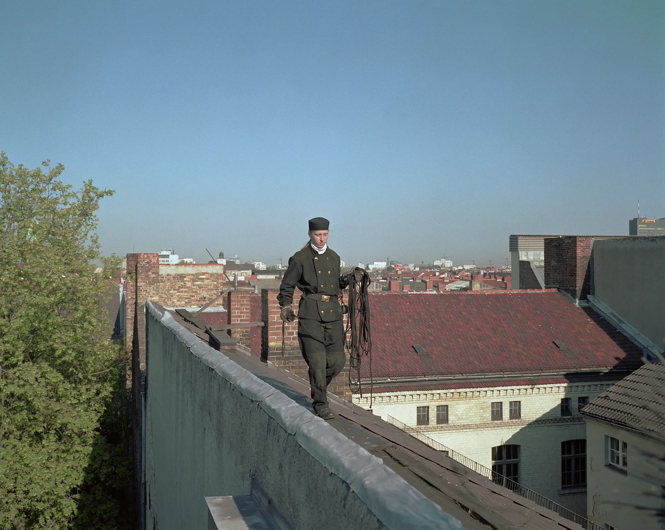 Chimney Sweeper in Berlin, Germany.
        Walking along the roofs, the chimney sweeper
        carries her tools in traditional uniform.